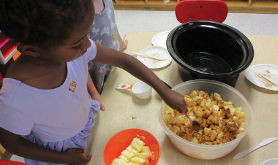 A child stirs food at the cooking table.