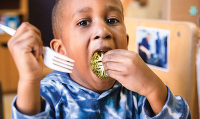 A child eats a piece of broccoli.