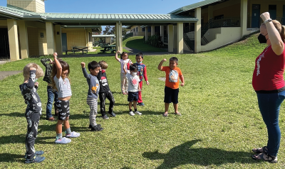 a teacher showing stretches to children outdoors