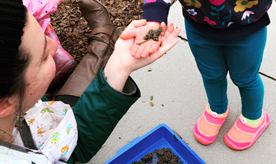 an adult handing a child a piece of mud with a worm in it