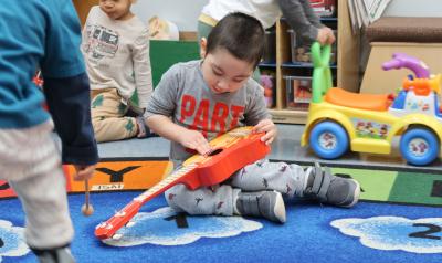A young child playing with a guitar in a classroom