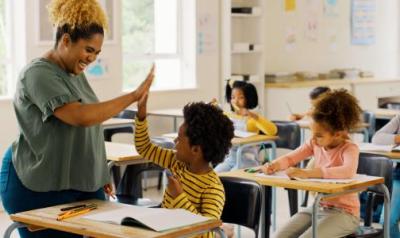 An educator high fiving a student in a classroom