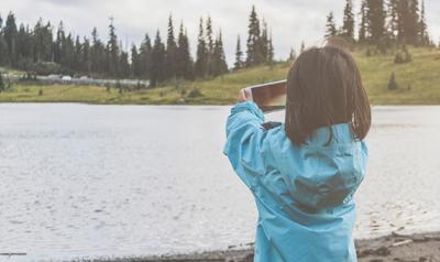 Child at a lake taking a photo with a smartphone