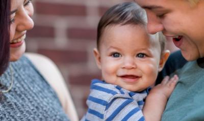 A couple smiles and embraces their toddler son.