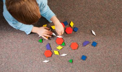 A preschooler plays with geometric shapes on a carpet