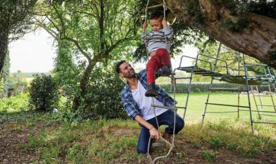 A father plays outside with their child on a rope ladder