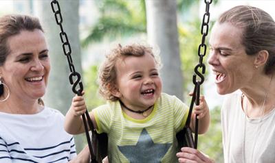 Two adults play with a young child on a swing