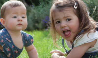 An infant and toddler laying in the grass outside