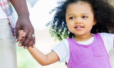 Girl holding hands with parents outside