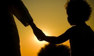 A child and a family member in silhouette against a setting sun.
