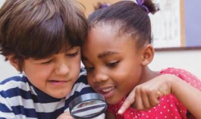 Two young children look through a magnifying glass together