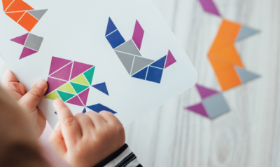A young child copies designs of various geometric shapes on a piece of paper.