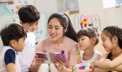 a teacher reading a book surrounded by children