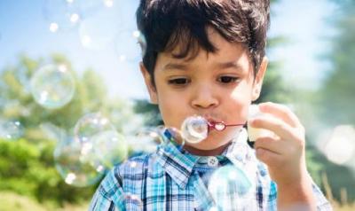 Preschool aged boy blowing bubbles outside