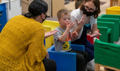 two teachers in face masks making hand gestures with a child
