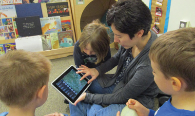 a teacher showing children a game on an ipad