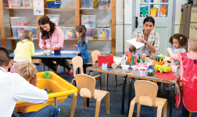 a classroom with multiple tables with children and teachers