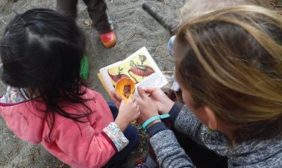 a teacher showing a child a nature book outside