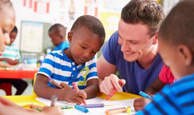 a teacher observing a child drawing with crayons