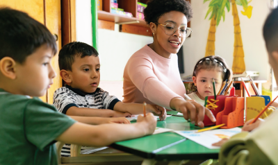 A teacher guides children as they color.