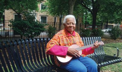 Ella Jenkins sitting on a bench with a guitar in her hands