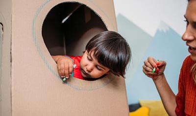 student playing in a cardboard fort with teacher