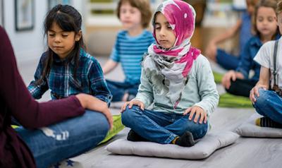 Students sits on mats and do meditation exercises with a teacher 