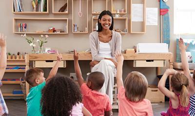 teacher smiling while student raise their hands to participate