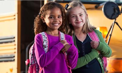 Two girls standing next to a school bus