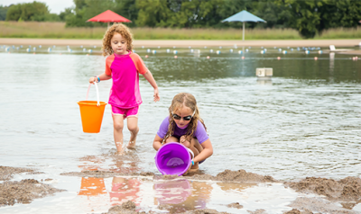 Two young girls at the lake scooping water into buckets