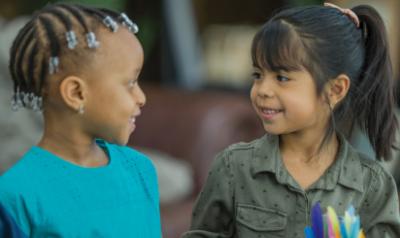 Two little girls smiling at one another.