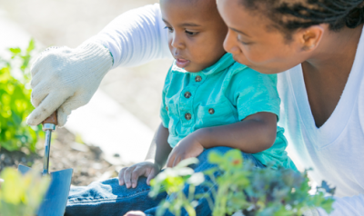 A young child in a garden with an adult.