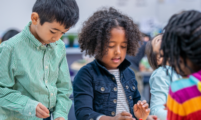 children discussing something at a table while writing