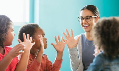 Teacher and three preschool students with hands up