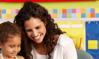 Teacher and young girl sitting at a desk in a classroom.