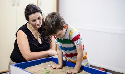  Teacher watching a young boy play in a sandbox