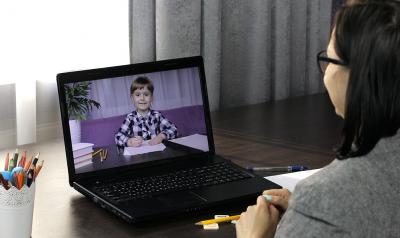 Teacher on a laptop smiling at young child