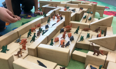 Children play with blocks and dinosaur figurines.