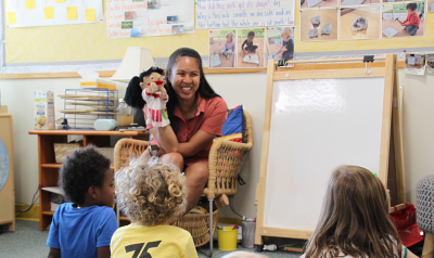 feature teacher cecilia fowler with children playing with a puppet