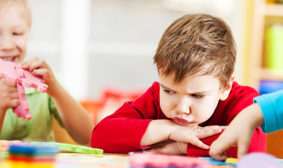 An unhappy child sitting at a table with others.