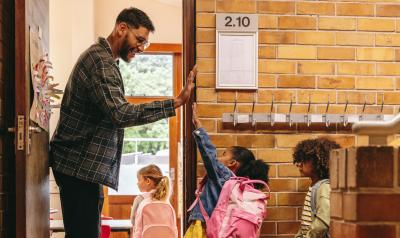 A male teacher high fiving a student on the way into the classroom