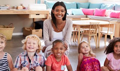 Group photo of teacher smiling with preschool students in classroom