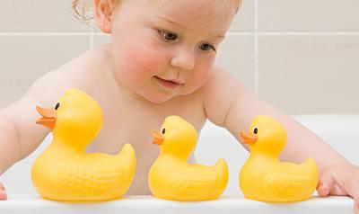 Toddler in the bathtub playing with rubber ducks.