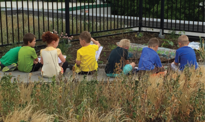 Row of children sitting outside near a garden