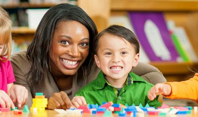 Teacher smiling with 3 young children playing blocks