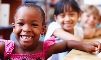 Three children smile while sitting at a table.