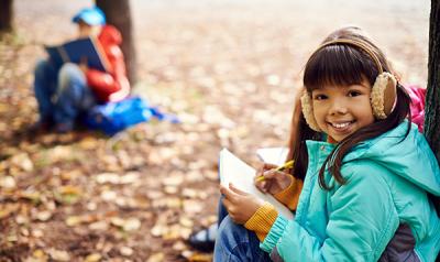 A young girl draws and takes notes in a forest