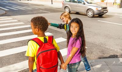 Three children of different races and ethnicities walk to school together.