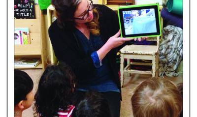 Teacher showing children a video of their previous day on a tablet.