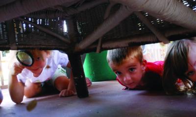 Children searching with magnifying glass under furniture. 